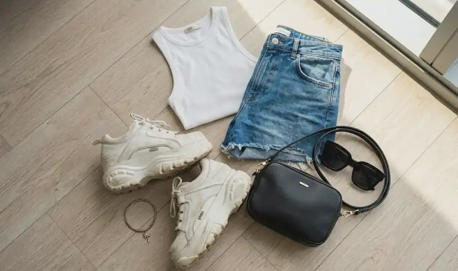 Festival outfit essentials flat lay sneakers bag sunglasses tank shorts