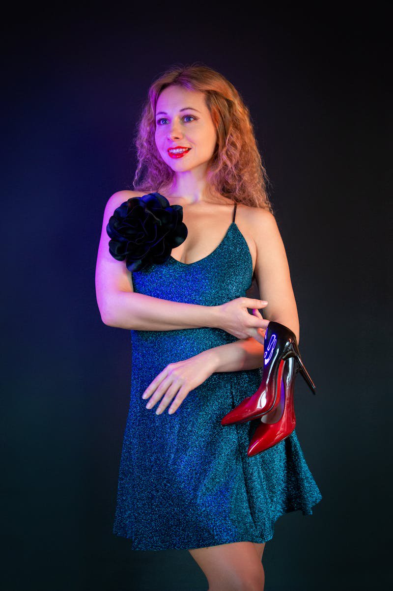 Stylish woman in blue evening dress with red heels posing elegantly against a backdrop