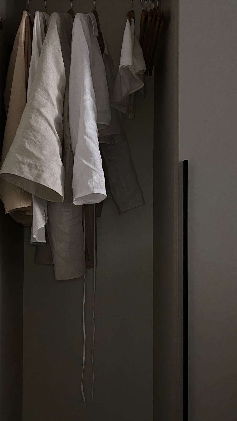 Linen clothes hanging neatly on wooden hangers in a softly lit closet