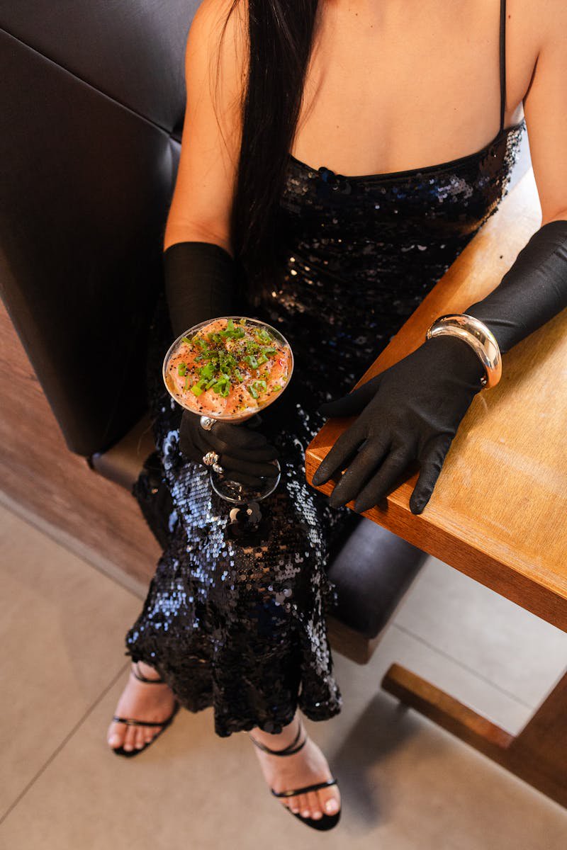 Elegant woman in black sequin dress holding a cocktail in a glamorous evening setting