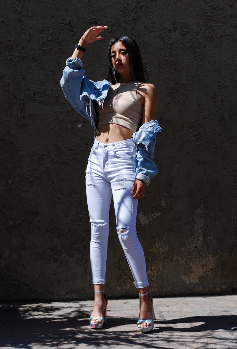 Fashionable woman in denim jacket and white jeans posing in warm sunlight outdoors