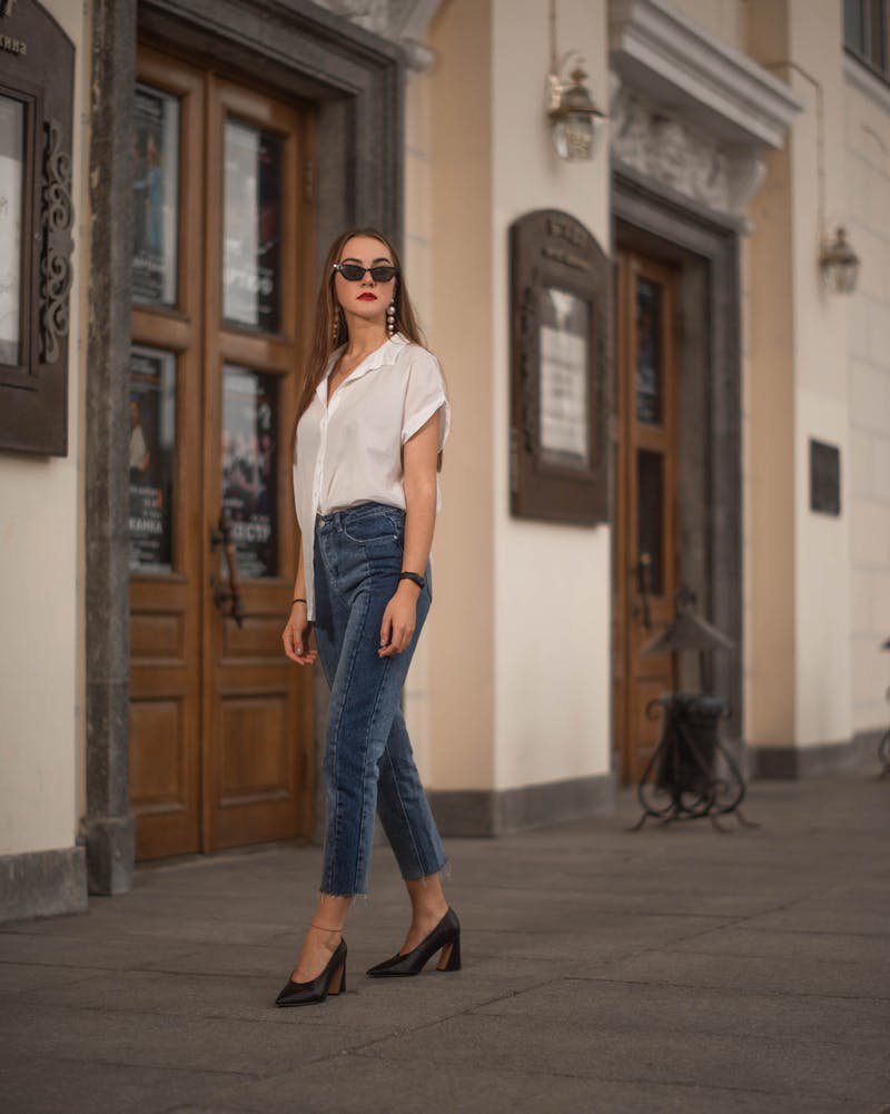 Fashionable woman in sunglasses and jeans posing by ornate wooden doors on a city street