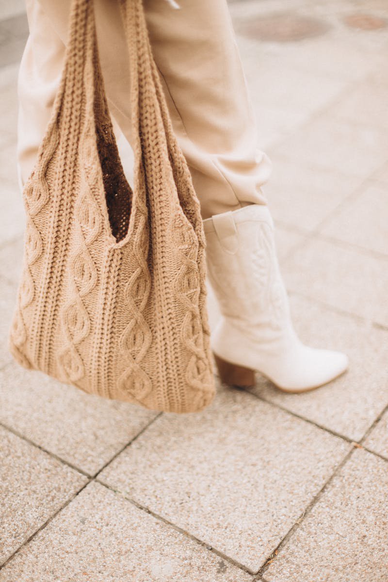 A well-chosen bag and shoe combination anchors an entire outfit before you add anything else Beige knit handbag and white boots on a city sidewalk in natural daylight