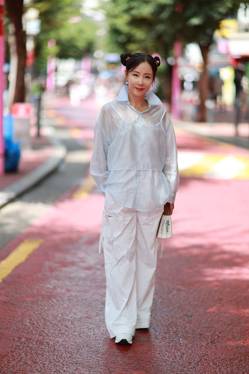 Fashionable woman in white outfit walking on a vibrant red street, Korean street style aesthetic
